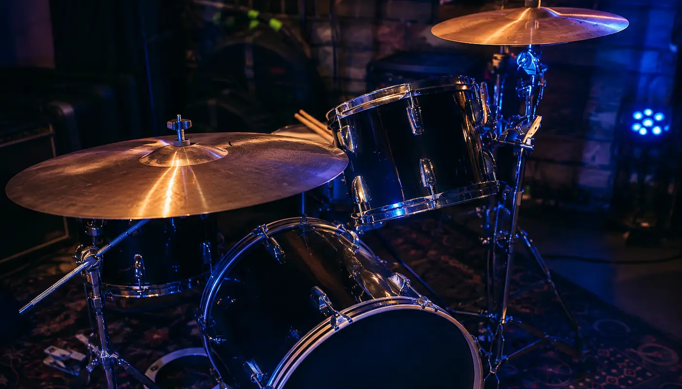 Baby drum set on a stage rug, lit blue, with the single cymbal stand and the clamp-mounted second cymbal visible.